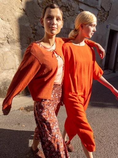 Two women wearing layers of clothes in shades of orange from Gudrun Sjödén.