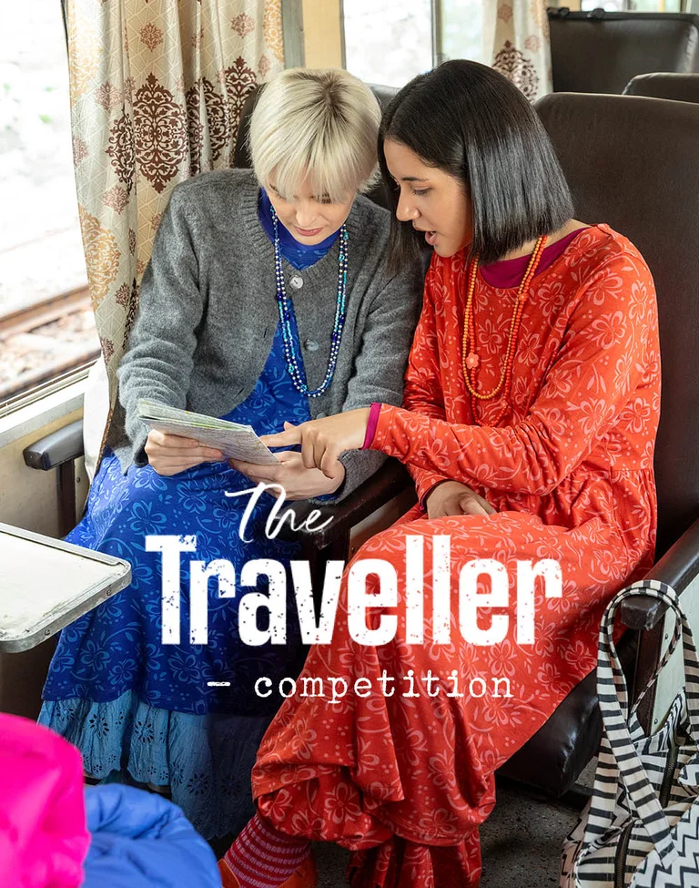 Two women on a train, leaning over a map, wearing layers of clothes from Gudrun Sjödén.