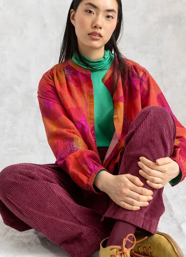 A seated woman wearing turquoise corduroy clothes from Gudrun Sjödén. 