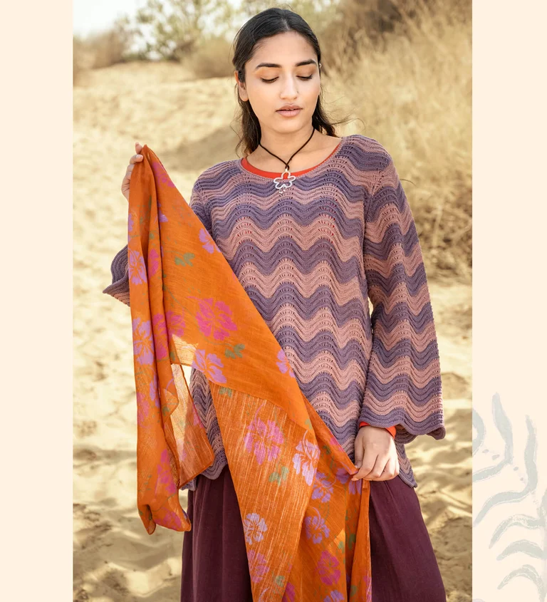 A woman wearing a knit sweater and holding a patterned shawl from Gudrun Sjödén.