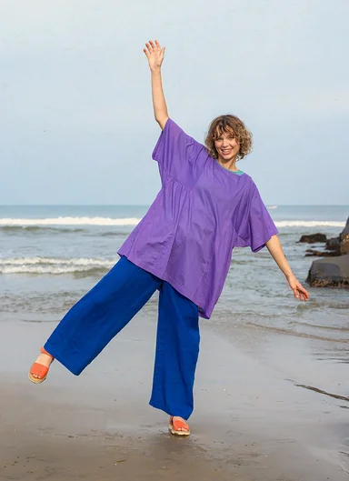 A woman on a beach wearing a purple tunic and blue trousers from Gudrun Sjödén.