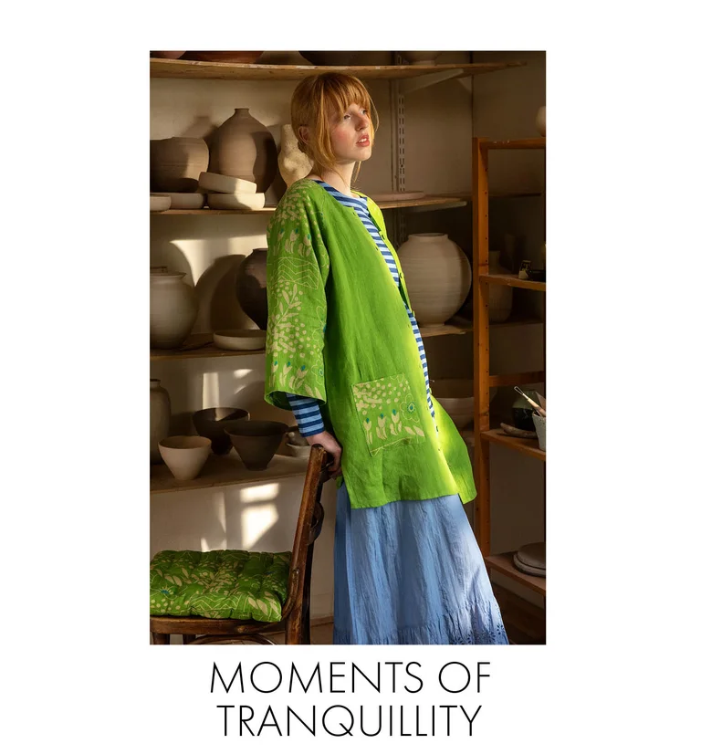 A woman in a pottery studio wearing a green “Nemorosa” linen tunic, a striped top and a light-blue skirt from Gudrun Sjödén.