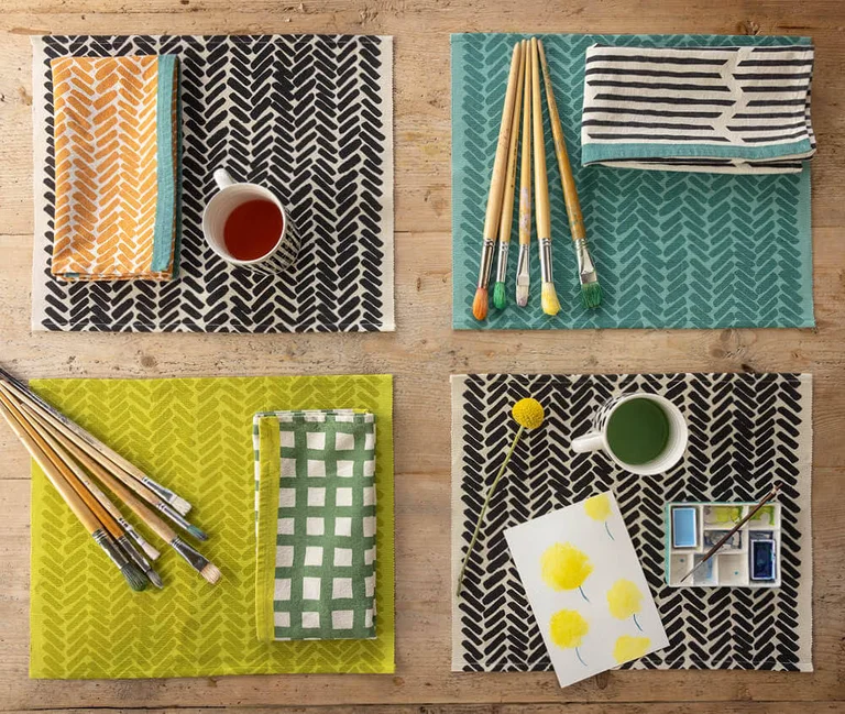 Une table avec quatre sets de table de différentes couleurs provenant de la collection d'hiver 2025 de Gudrun Sjödén.