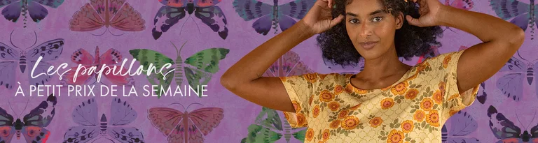Une femme portant une robe jaune à motifs se tient devant un mur violet avec des papillons.
