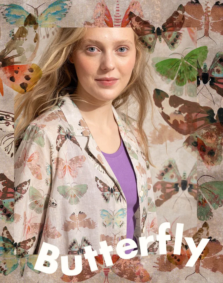 A woman in front of a butterfly background wearing a beige dress with a butterfly pattern from Gudrun Sjödén.