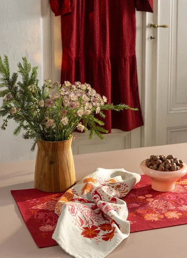 A tablescape in warm hues with flowers and red textiles from Gudrun Sjödén’s Alaska Home collection.
