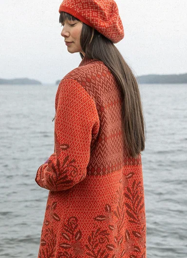 Eine Frau in einer orangefarbenen Langstrickjacke von Gudrun Sjödén. 