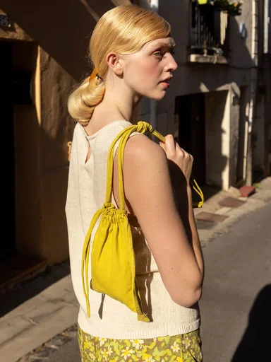 A woman wearing a sleeveless top and patterned skirt from Gudrun Sjödén, with a yellow bag over her shoulder in a sunny urban setting.