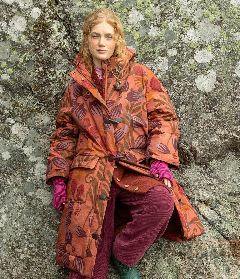 Eine Frau in einer orangefarbenen gemusterten Winterjacke von Gudrun Sjödén. 