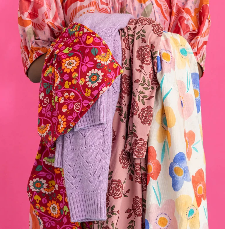 A woman holding floral clothes from Gudrun Sjödén.  