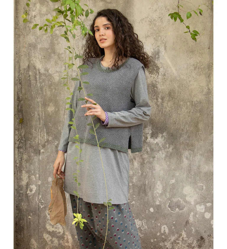 A woman wearing a gray knit sweater vest and jersey tunic from Gudrun Sjödén.