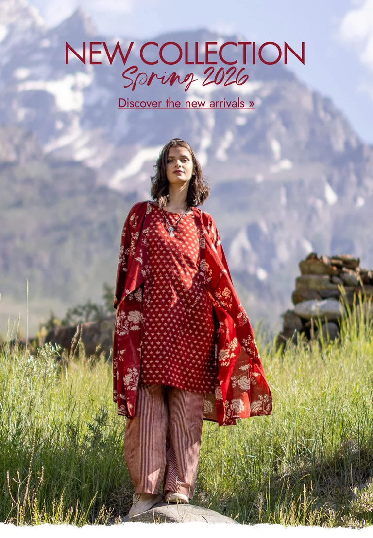 A woman standing in a mountain landscape wearing layers of red, woven clothes from Gudrun Sjödén.