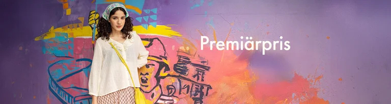 A woman standing by a wall wearing a ruffled blouse from Gudrun Sjödén. 