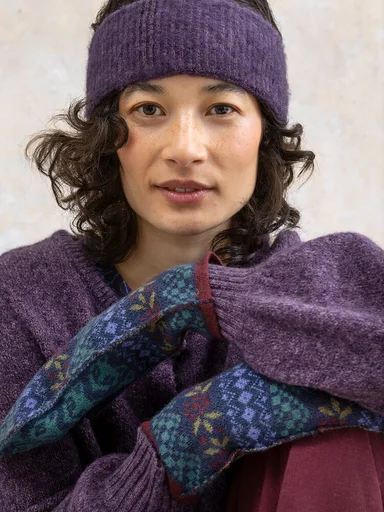 Eine Frau in einem gestrickten Stirnband und gemusterten Fäustlingen von Gudrun Sjödén. 