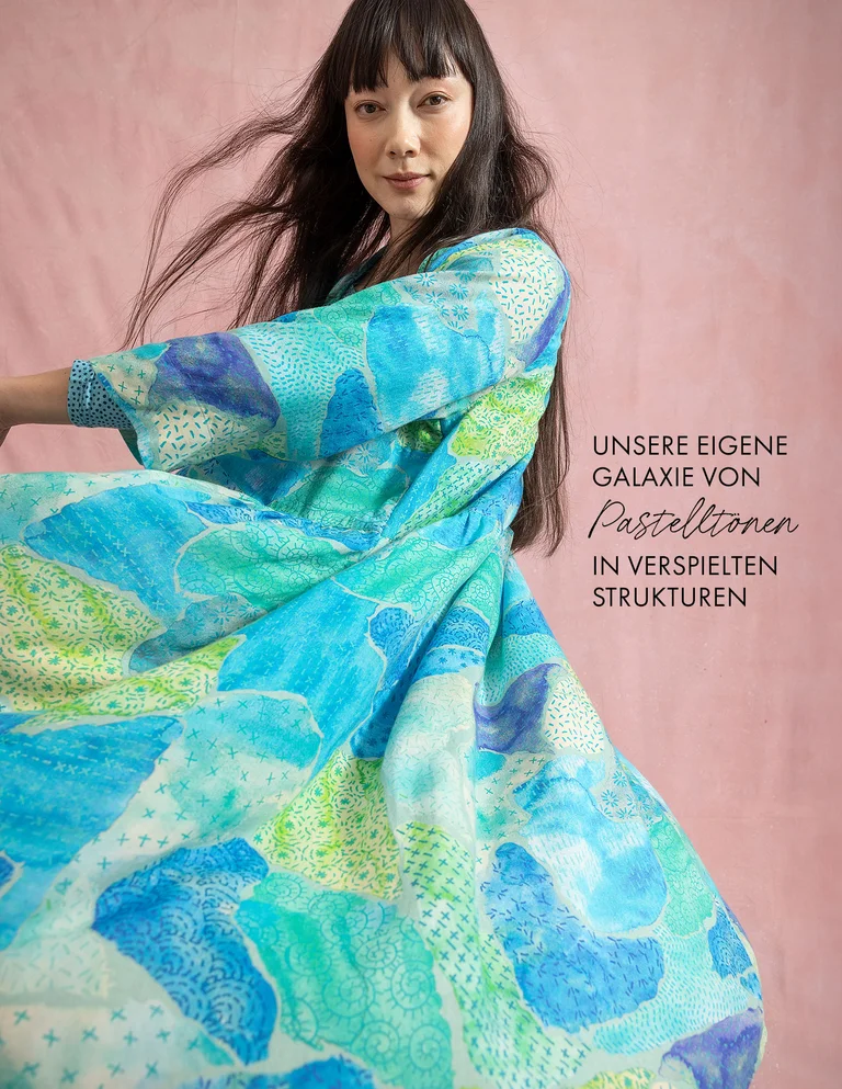 Eine Frau in einem blau-grün gemusterten Kleid von Gudrun Sjödén.