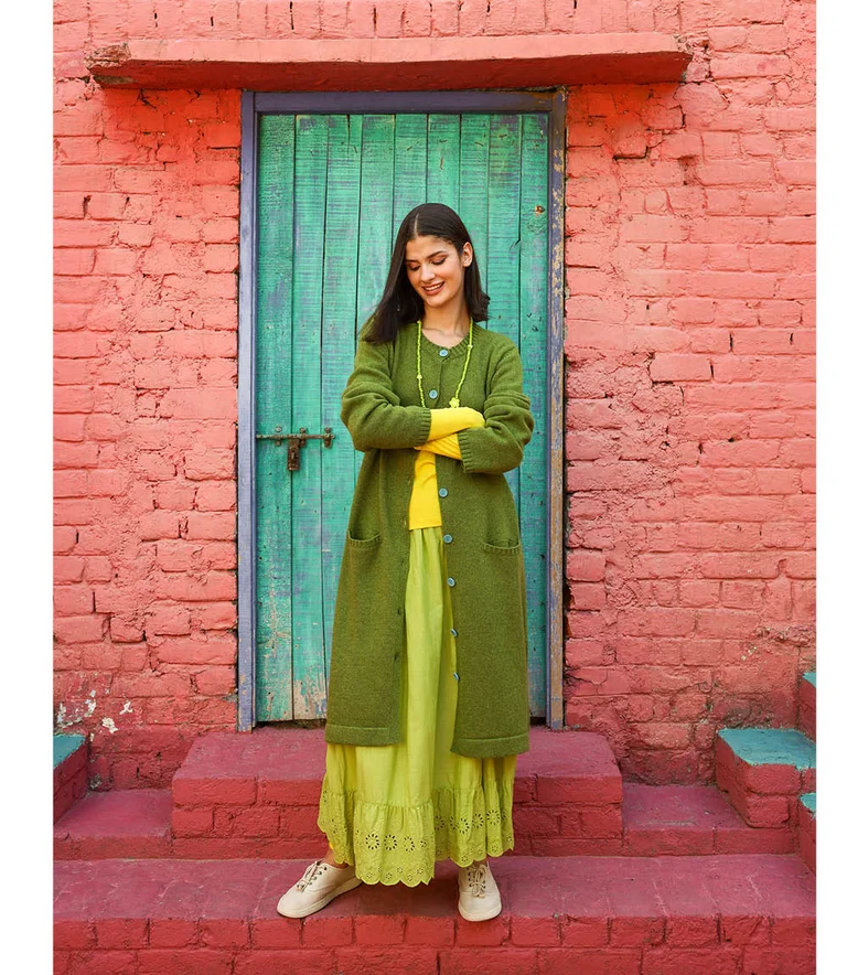 A woman posing in front of a door wearing layers of green and yellow clothes from Gudrun Sjödén. 