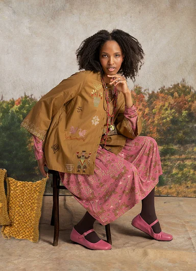 A woman sitting on a chair wearing layers of clothes from Gudrun Sjödén.