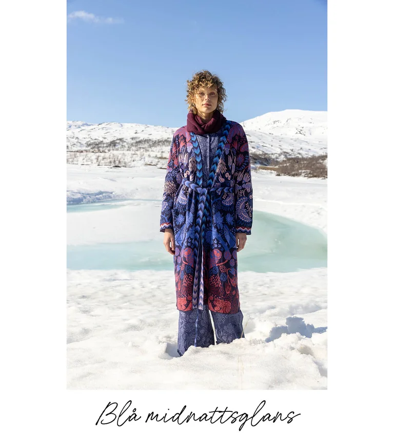 En kvinna som står i ett snölandskap iklädd lager på lager av kläder från Gudrun Sjödéns julkollektion 2025.