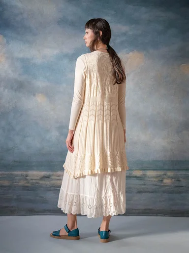A woman wearing a light layered dress from Gudrun Sjödén, photographed from behind against a painted sea background.