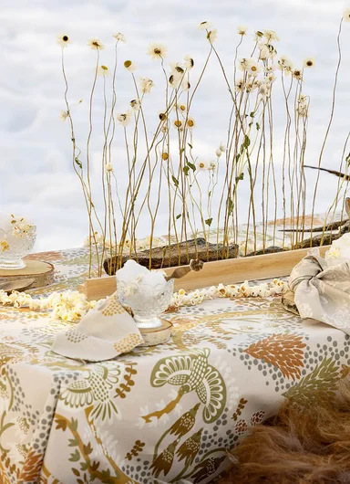 A tablescape in warm hues with flowers and red textiles from Gudrun Sjödén’s Alaska Home collection.