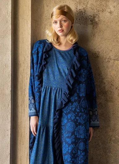 A woman leaning against a wall wearing layers of blue clothes from Gudrun Sjödén.