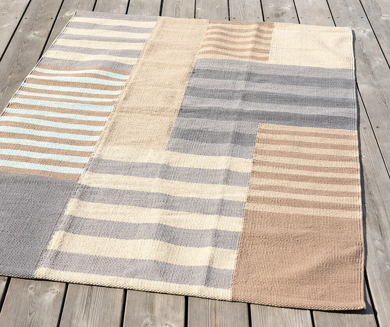 A beige-grey mat from Gudrun Sjödén with a mixed pattern of stripes. The mat is on a jetty.