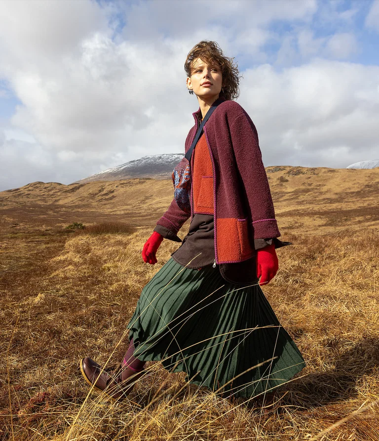 A woman walking in a mountain setting wearing layers of clothing from Gudrun Sjödén.