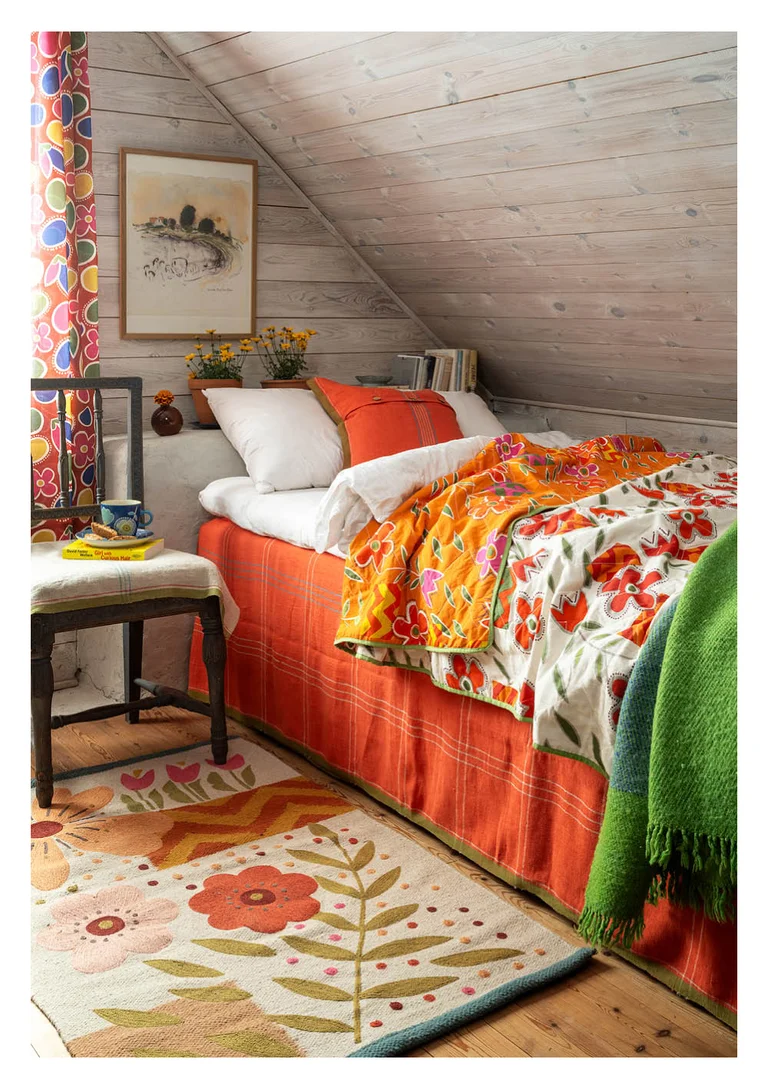 An attic bedroom with a quilted bedspread and a checked tablecloth in chili as a bed skirt, from Gudrun Sjödén.