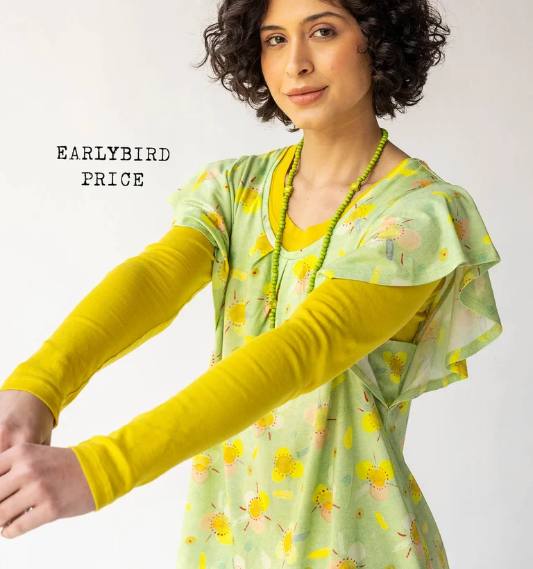 A woman dressed in a patterned green jersey-fabric top, worn over a yellow long-sleeved top from Gudrun Sjödén.