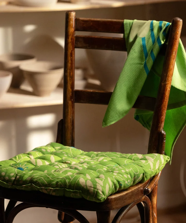 A green seat cushion and kitchen towel from Gudrun Sjödén on a wooden chair.