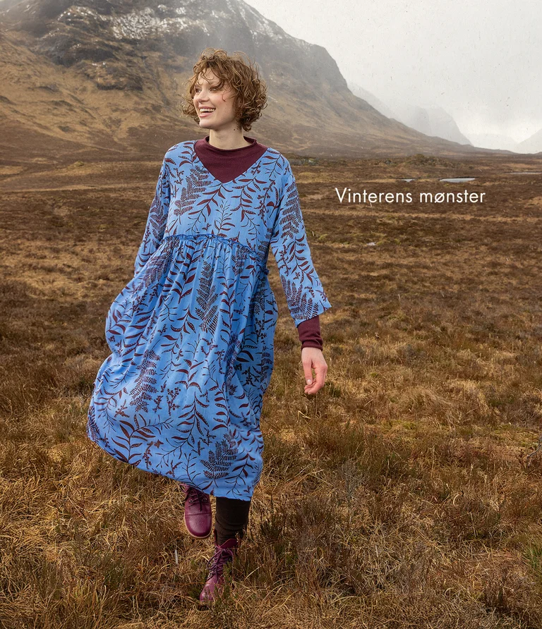 A woman walking in a mountain setting wearing a blue patterned dress from Gudrun Sjödén.