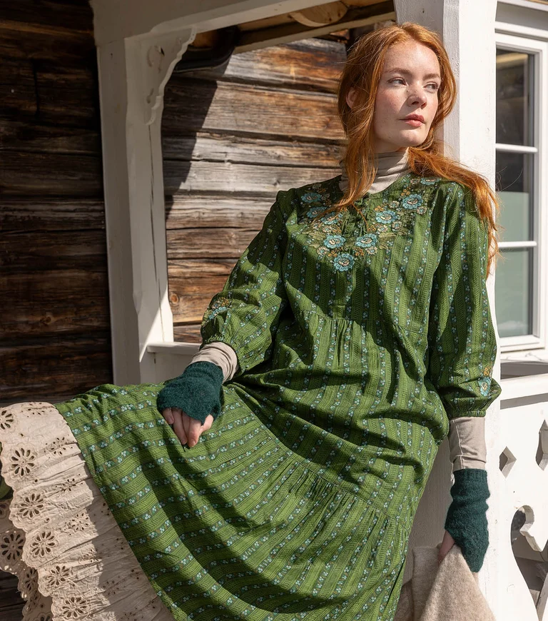 A woman wearing layers of green and beige clothes from Gudrun Sjödén’s 2025 Christmas collection.  