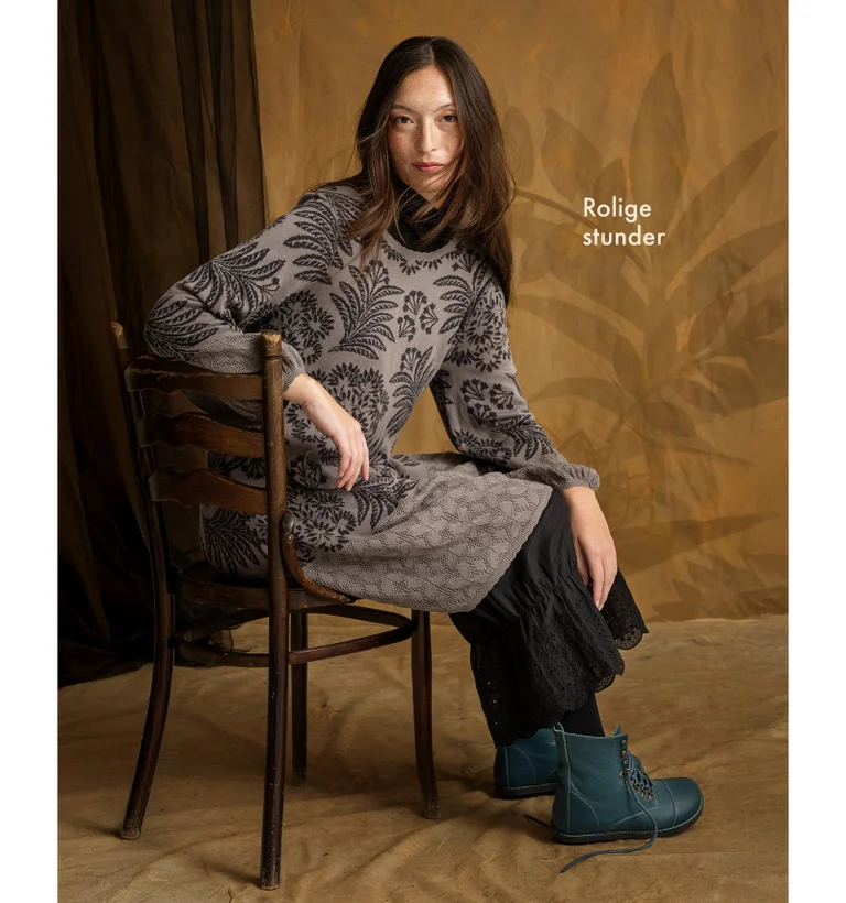 A woman sitting on a chair wearing a knit dress in shades of gray from Gudrun Sjödén.