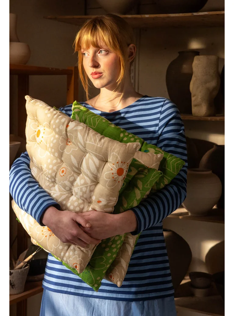 A woman holding several seat cushions from Gudrun Sjödén in her arms.