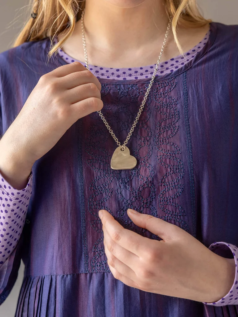 A close-up of a woman wearing a garment with embroidered yoke and a silver necklace from Gudrun Sjödén’s 2025 Christmas collection. 