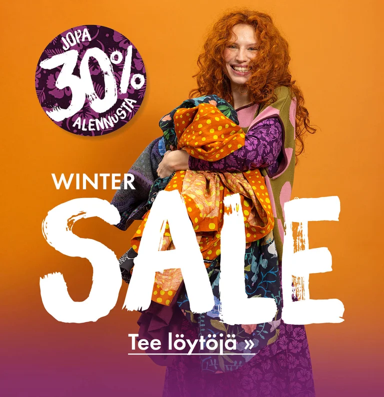 Nainen, jolla on syli täynnä Gudrun Sjödénin värikkäitä vaatteita.