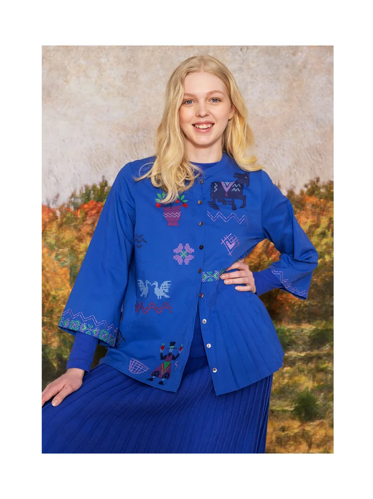 A woman wearing a bright blue blouse with embroidery from Gudrun Sjödén.