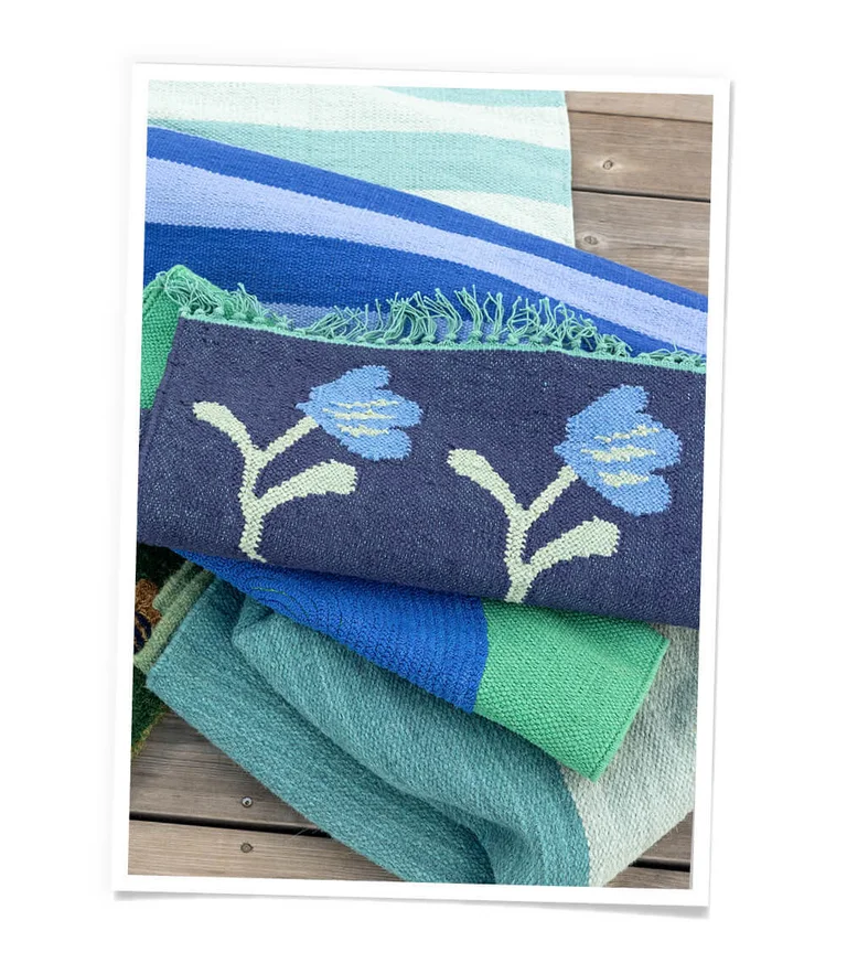 A close-up of different mats in shades of blue from Gudrun Sjödén, in a pile on a jetty.