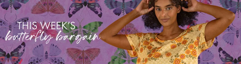 A woman in a patterned yellow dress stands in front of a purple wall with butterflies.