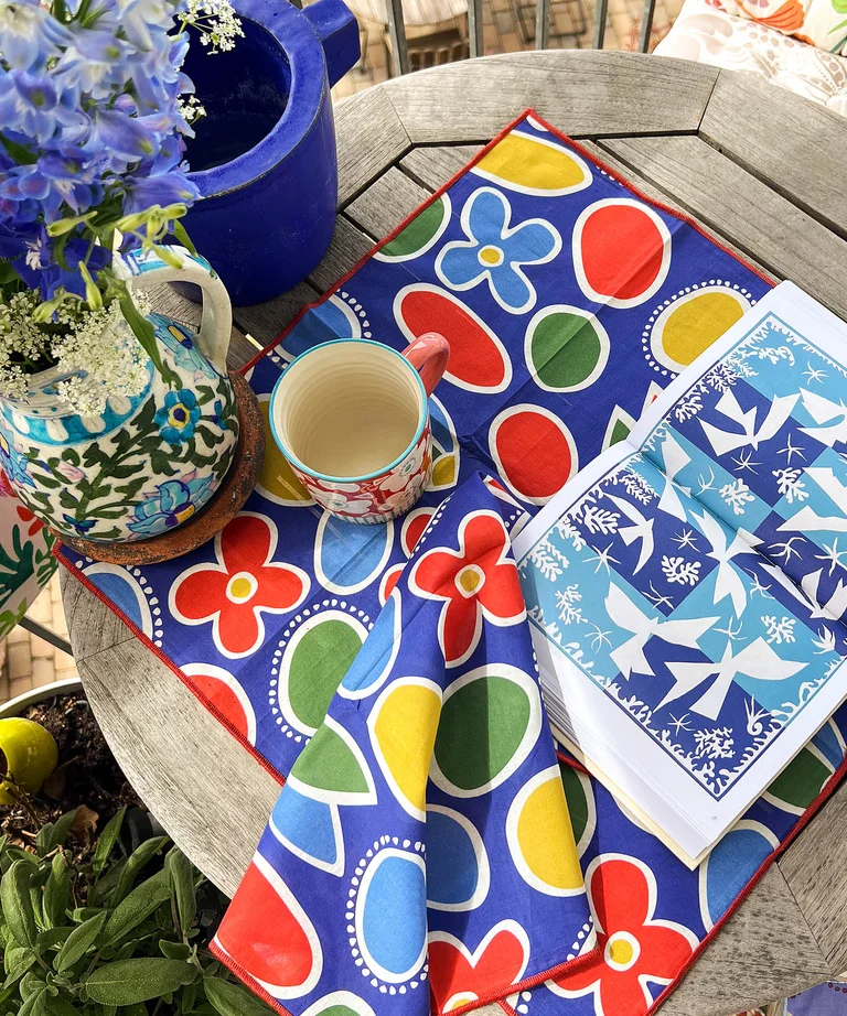 Patterned cloth napkin in cobalt blue from Gudrun Sjödén on a round wooden table on a balcony.