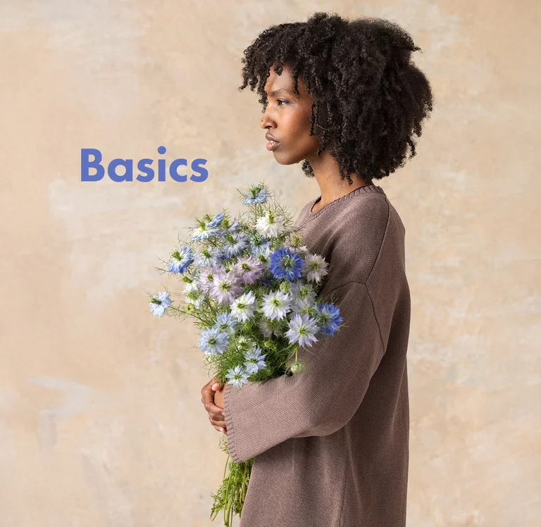 Eine Frau mit einem Blumenstrauß, in einem braunen Basic-Pullover von Gudrun Sjödén.