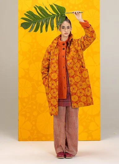 A woman walking next to the water wearing white, embroidered clothes from Gudrun Sjödén.