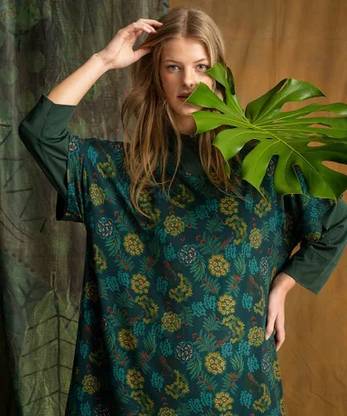 A woman with a leaf in front of her face wearing a floral tunic from Gudrun Sjödén.