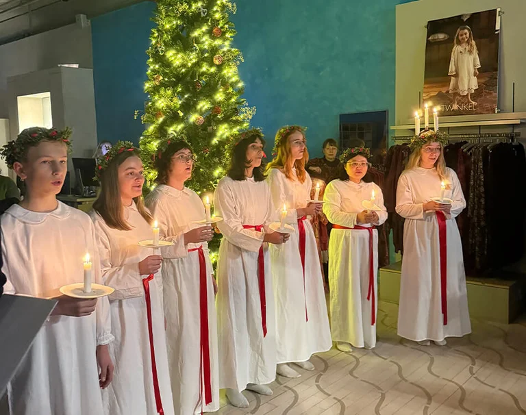 Et Lucia-tog som står og synger ved et stort juletre i en av Gudrun Sjödéns butikker.