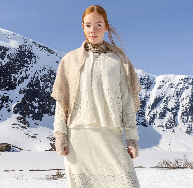 Eine Frau in verschneiter Landschaft, im Lagenlook in Beige und Weiß aus Gudrun Sjödéns Weihnachtskollektion 2025. 