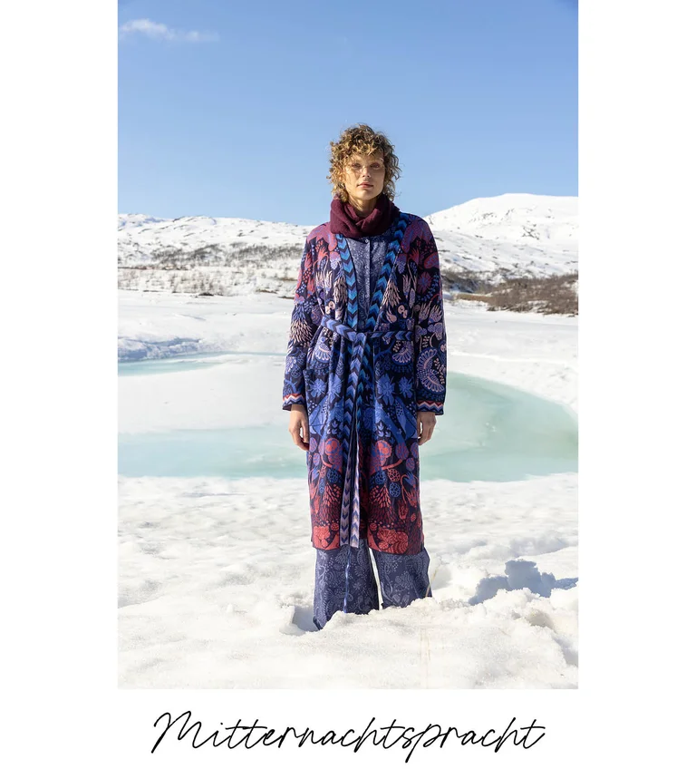 Eine Frau in verschneiter Landschaft, im Lagenlook mit Mode aus Gudrun Sjödéns Weihnachtskollektion 2025.