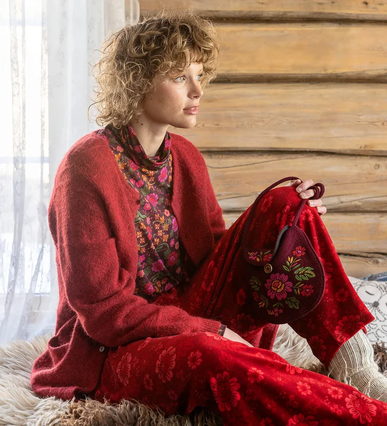 A woman sitting down wearing layers of red clothes from Gudrun Sjödén’s 2025 Christmas collection.