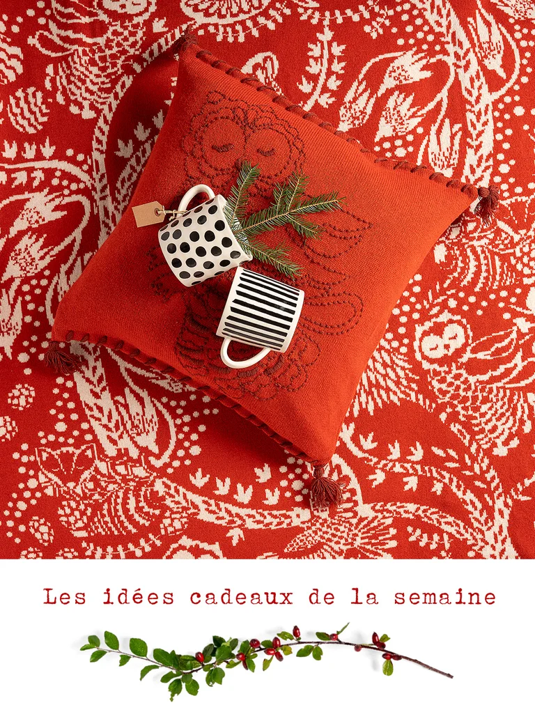 Deux tasses en céramique noire et blanche sur un coussin rouge brodé de la collection de Noël 2025 de Gudrun Sjödén. 