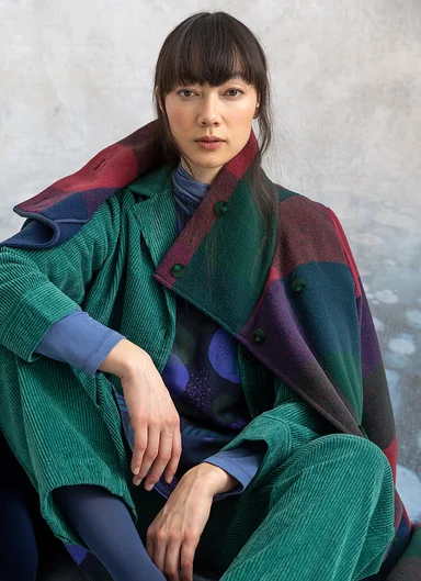 A seated woman wearing turquoise corduroy clothes from Gudrun Sjödén. 