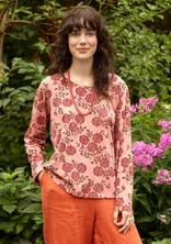 Rosa Langarm-Shirt mit roten Blumen. Das Model trägt dazu eine Hose in orange.